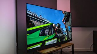 The Philips 65OLED908 TV on a TV stand. On screen is a Nascar racing driver looking out of the window of a car.