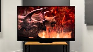 The Panasonic MZ2000 TV on a TV stand with a couple of stegosauruses on screen.
