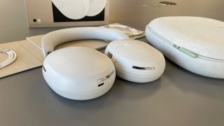 Sonos Ace noise-cancelling headphones lying flat next to case on grey surface